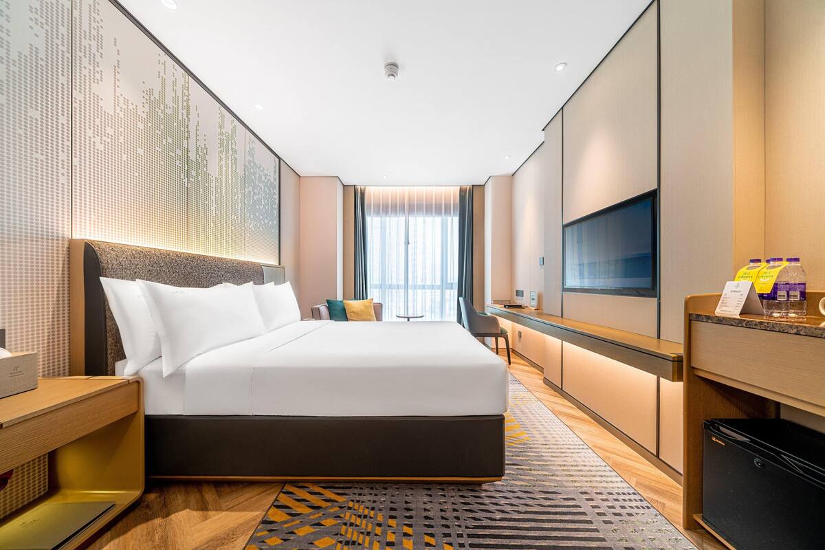 A hotel room with a large bed, a desk, a TV, and a minibar.