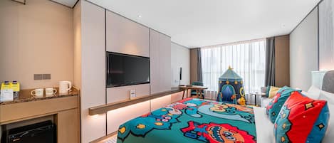 A hotel room with a bed, a TV, a desk, a minibar, and a window with curtains.
