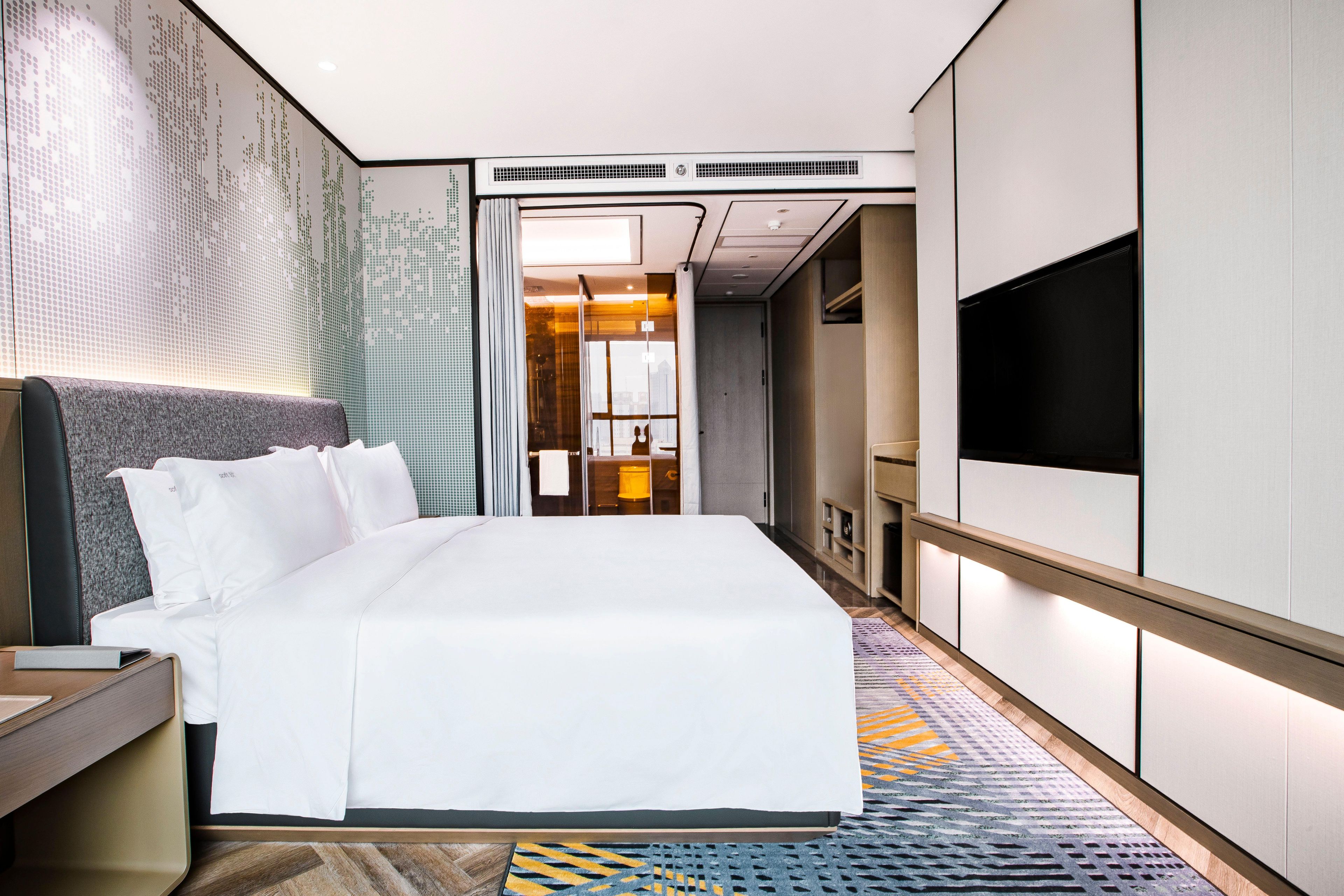 A modern hotel room with a large bed, a flat-screen TV, a desk, and a walk-in closet.