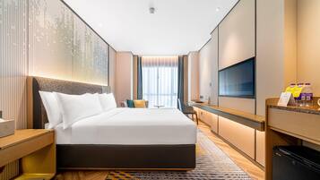 A hotel room with a large bed, a desk, a TV, and a minibar.