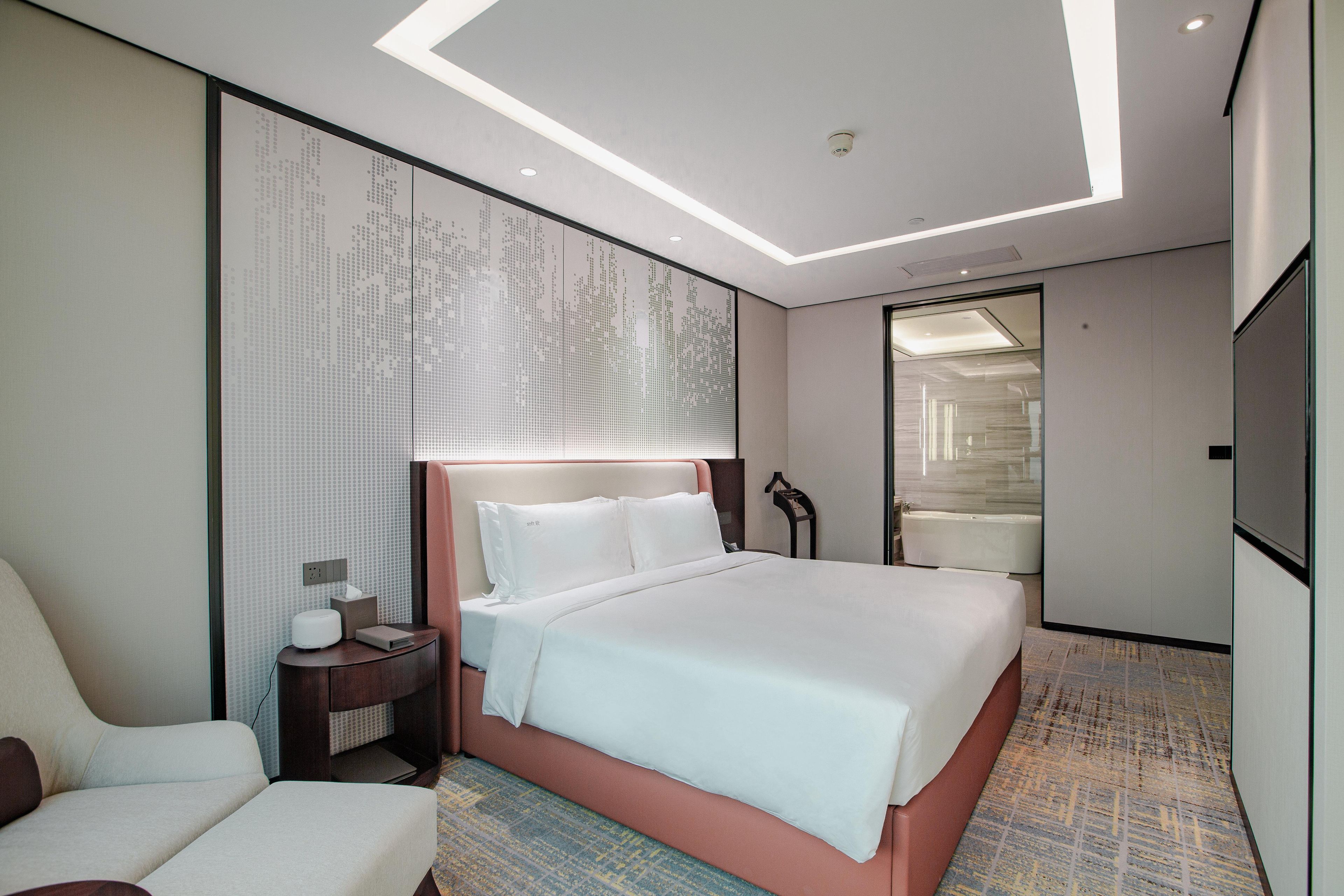 Una habitación de hotel moderna con una cama grande, una mesita de noche, una silla y un espejo amplio.