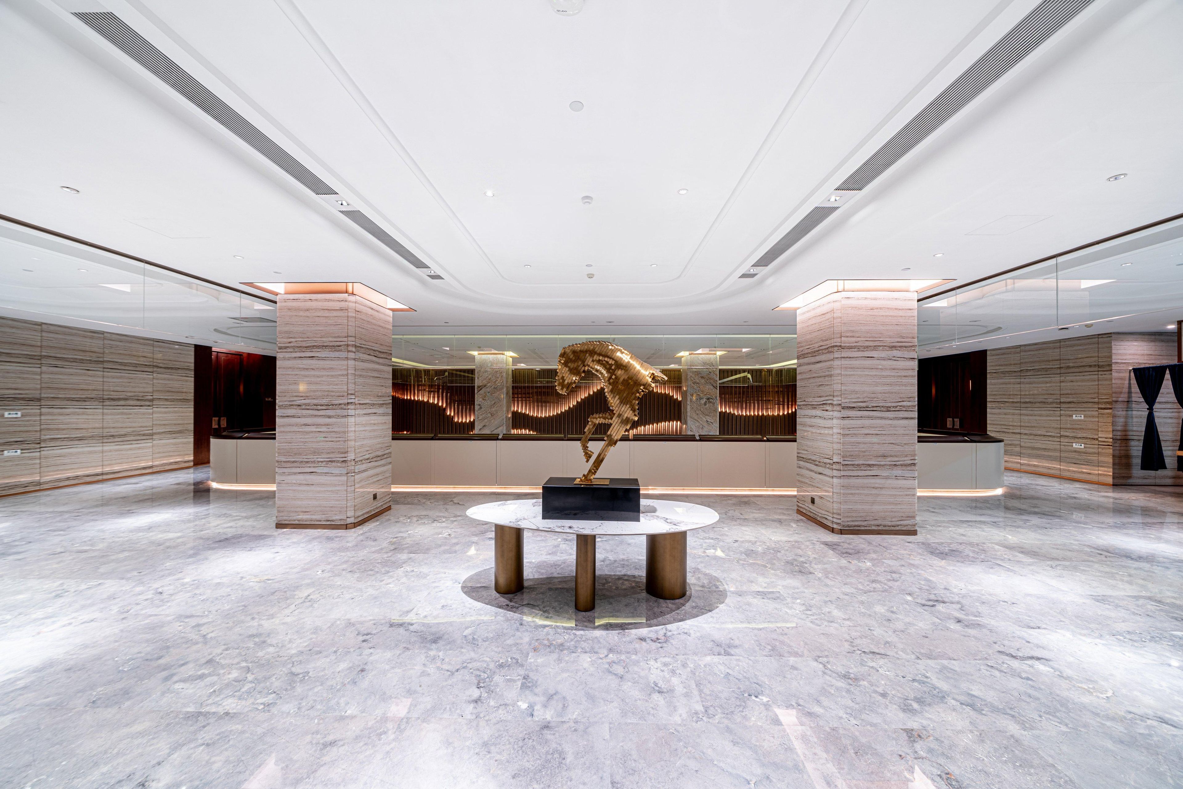 A spacious lobby with a marble floor, a central round table, and a large abstract sculpture.
