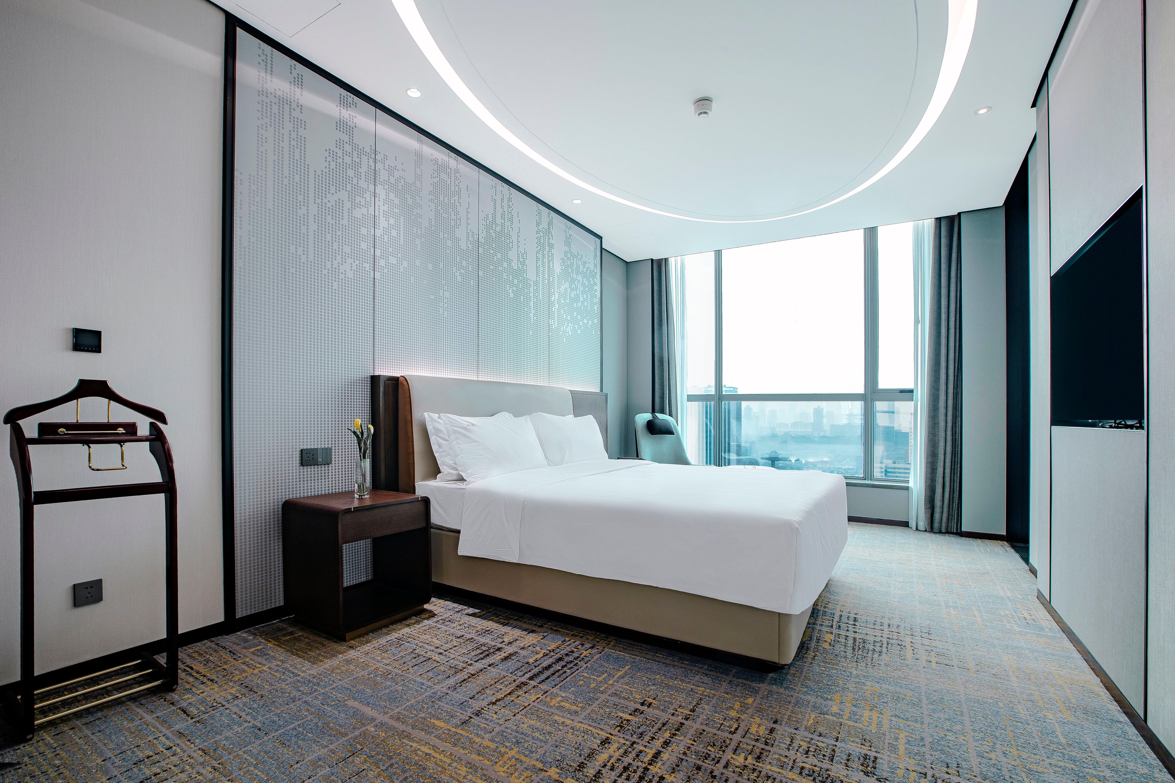 Een moderne hotelkamer met een groot bed, een nachtkastje, een wandtelevisie en uitzicht op de stad.