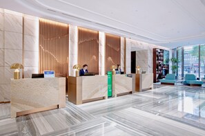 A modern hotel reception area with marble flooring, wooden reception desks, and a view of the city through large windows. - Holiday Inn Taiyuan City Center (Taiyuan)