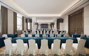Un salón de conferencias con filas de mesas y sillas, ventanas amplias y un escenario con una pantalla.