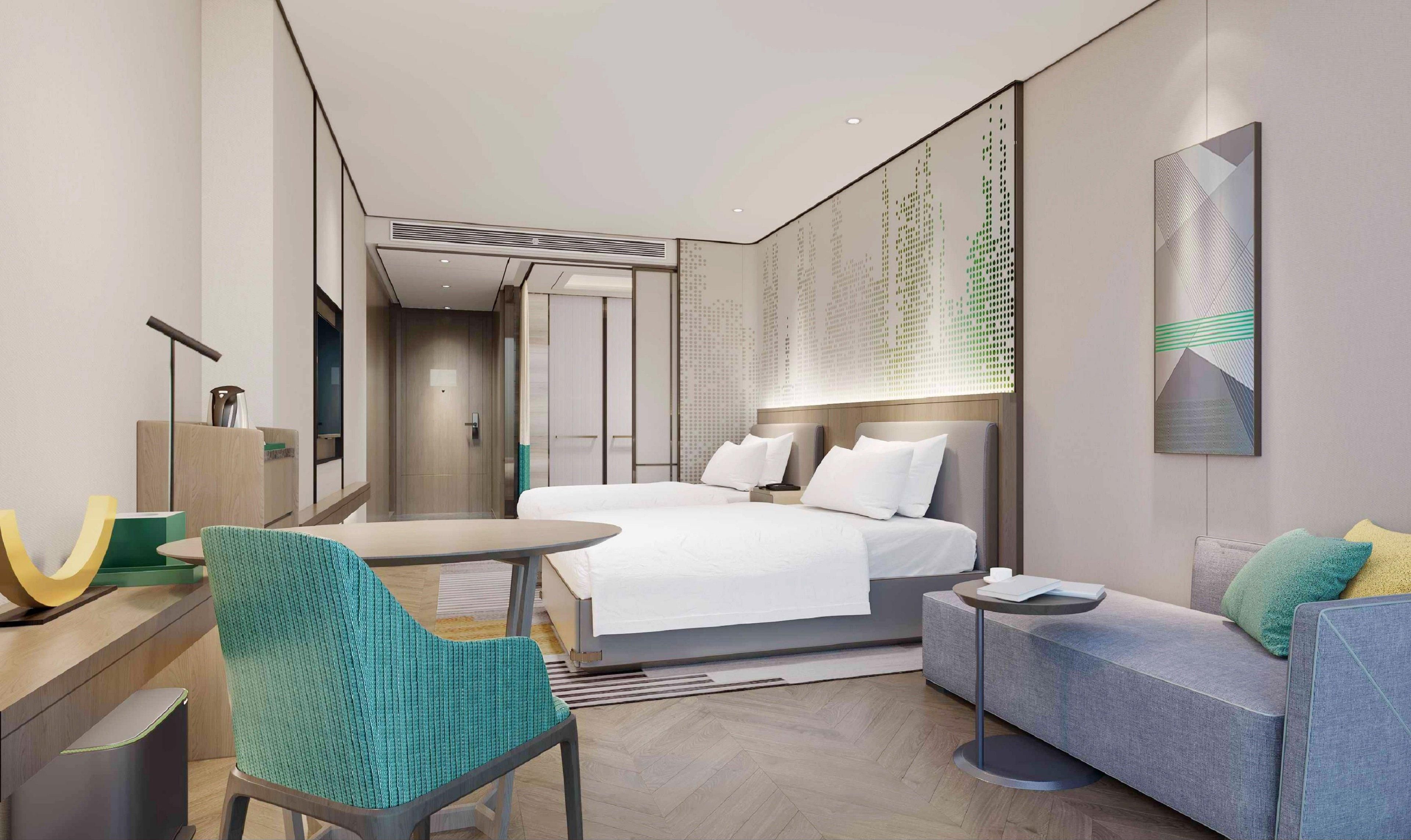 A modern hotel room with a bed, a desk, a chair, a sofa, and a wall-mounted artwork.