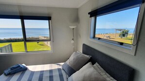 A bedroom with a large bed, two windows, and a view of the sea. - The Gin Trap (Pukehina)