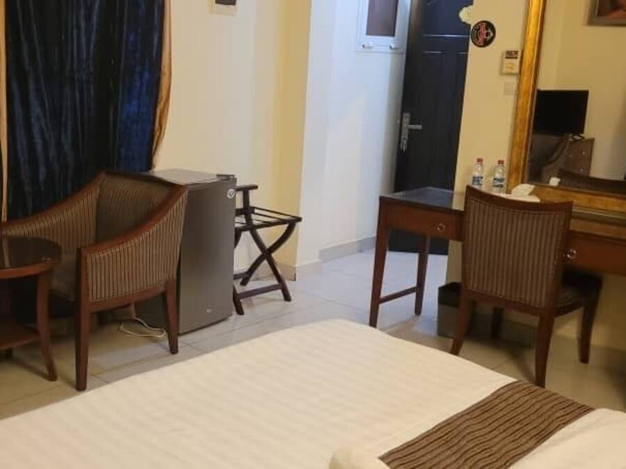 A hotel room with a bed, two wooden chairs, a small desk, a mirror, and a dark-colored curtain.