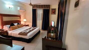 A hotel room with a bed, two bedside tables with lamps, a desk, a chair, a TV, and a ceiling fan.