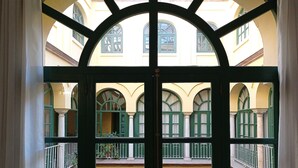 Une vue à travers une fenêtre à cadre noir, donnant sur une cour intérieure avec des arcades et un bâtiment jaune.