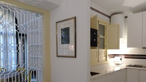 Une cuisine avec des meubles blancs, un four à micro-ondes et une fenêtre ornée d’une grille métallique décorative.
