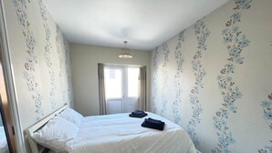 A bedroom with a bed, a window, and floral wallpaper. - 1 Bedroom Holiday Apartment - Flat 14 (Skegness)