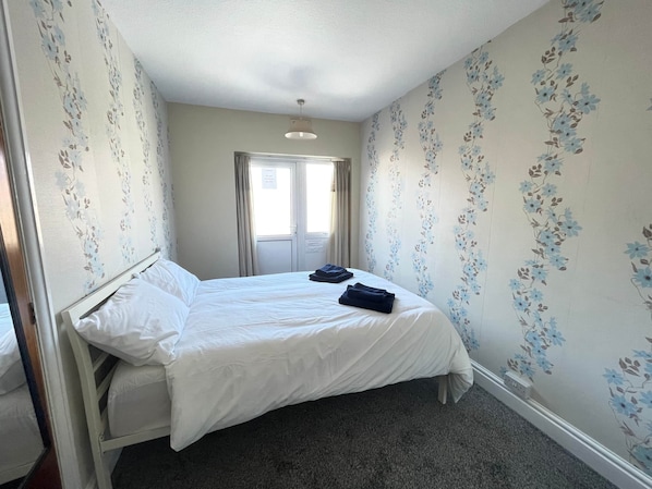 A bedroom with a bed, a window, and floral wallpaper.