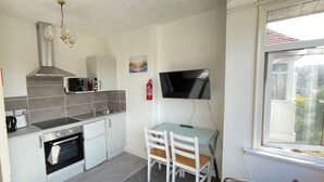 A compact kitchen with a stove, microwave, and sink. A TV is mounted on the wall, and a window provides natural light. - 1 Bedroom Holiday Apartment - Flat 14 (Skegness)