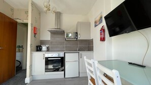 A compact kitchen with a microwave, oven, and a small dining area with a chair and table. - 1 Bedroom Holiday Apartment - Flat 14 (Skegness)