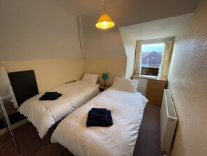 A hotel room with two beds, a window with a mountain view, a desk with a lamp, and a radiator. - 2 Bedroom Holiday Apartment Skegness - Flat 17 (Skegness)