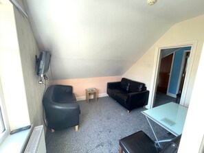 A small, compact living space with a black leather sofa, a glass coffee table, and a television mounted on the wall. - 2 Bedroom Holiday Apartment Skegness - Flat 17 (Skegness)