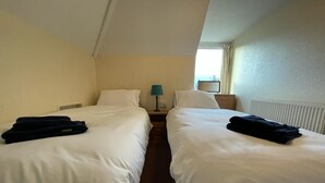 Une chambre d’hôtel avec deux lits simples, une table de chevet avec une lampe et une fenêtre avec des rideaux.