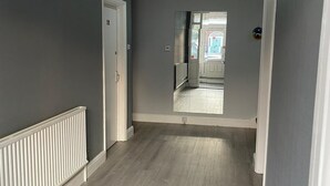 Un couloir aux murs gris, aux boiseries blanches et au plancher en bois. Il y a une porte sur la gauche et une porte au fond du couloir.