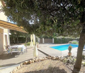 A pool area with a wooden deck, a table with chairs, and a potted plant.