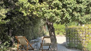 A garden area with two wooden chairs and a table, surrounded by trees and a gravel path.