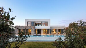 Et moderne hus med to etager, swimmingpool, stenfacade og store vinduer.