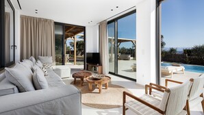 En moderne stue med sofa, sofabord, stole, fjernsyn og udsigt til en swimmingpool.