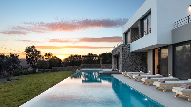 Et moderne hus med swimmingpool, liggestole og en stenvæg.