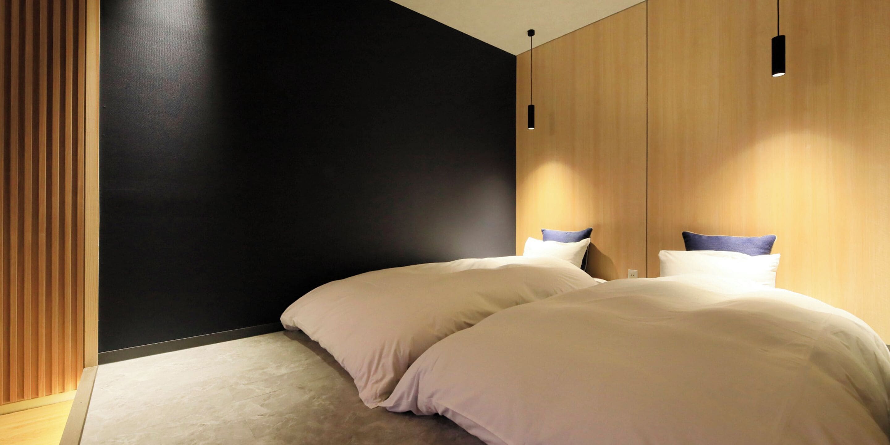 A modern bedroom with two beds, a dark accent wall, and wooden paneling.
