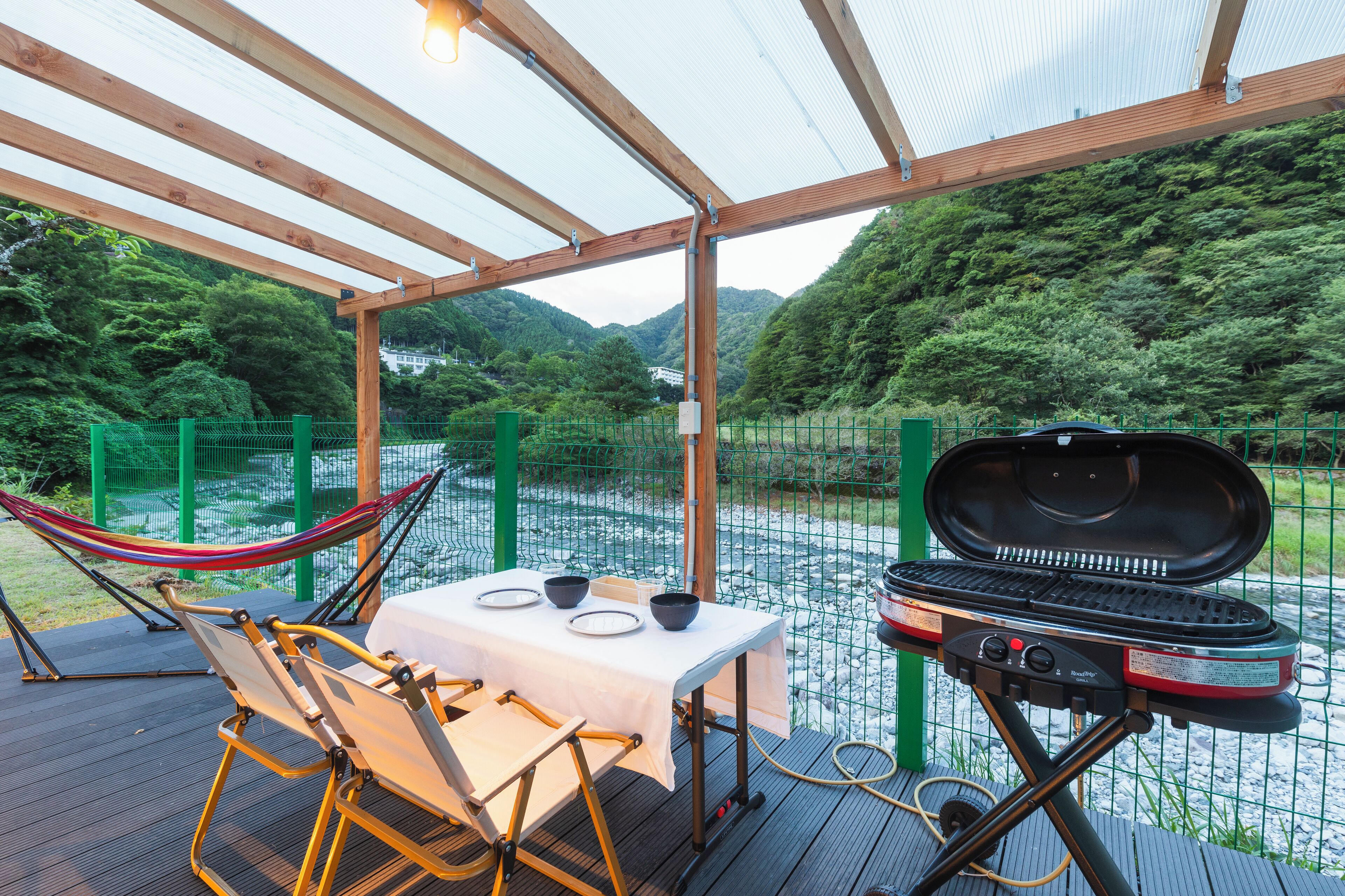 An outdoor dining area with a grill, chairs, and a table set for two.