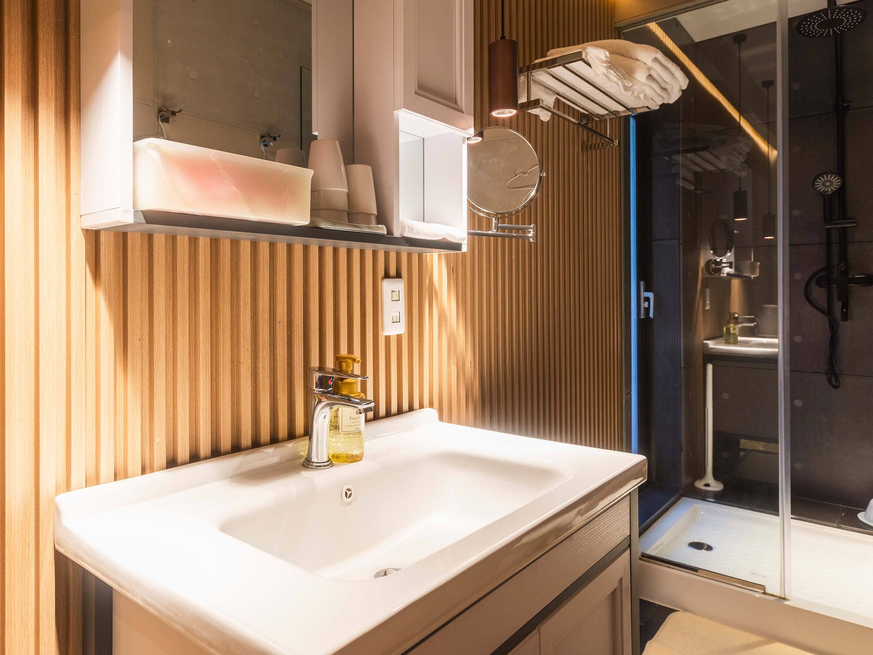A modern bathroom with a wooden panel wall, a white sink with a chrome faucet, a mirror, and a glass shower enclosure.