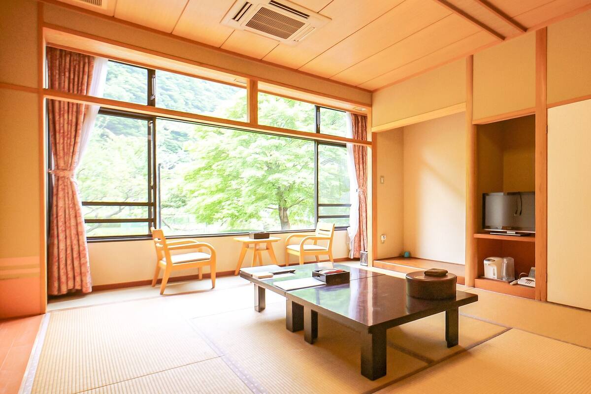 Een traditionele Japanse kamer met tatami vloeren, een lage tafel, stoelen, een televisie en schuifdeuren.