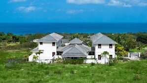 A coastal property with multiple white buildings, a grassy foreground, and a view of the ocean. - Infinity House | Ultra-Luxury Sea View Estate in Calijanda, Barbados (Holetown)