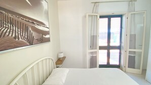 A bedroom with a bed, a nightstand, a lamp, a window with curtains, and a painting on the wall.