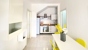 A modern kitchen with white cabinets, a stove, and a sink. There is a dining table with yellow chairs and a vase of flowers.