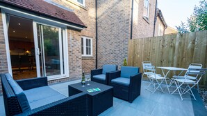 An outdoor patio with wicker furniture, a table with a bottle and glass, and a wooden fence. - Stylish, City Centre 3-bed House With Parking (Canterbury)