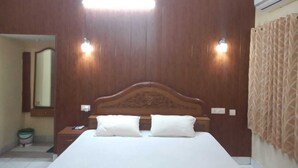 Habitació d'hotel amb un capçal de llit de fusta, dues làmpades de nit, un llit gran amb roba de llit blanca i un mirall a la paret esquerra.