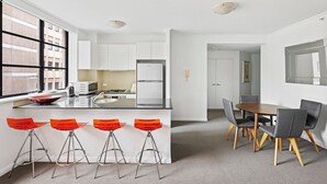 A modern kitchen with white cabinets, a central island with stools, and a dining area with a wooden table and chairs. - Central modern North Sydney 2 bed apartment with gym and pool (North Sydney)