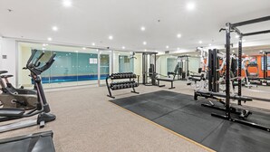 A gym with exercise equipment, a mirror, and a swimming pool in the background. - Central modern North Sydney 2 bed apartment with gym and pool (North Sydney)