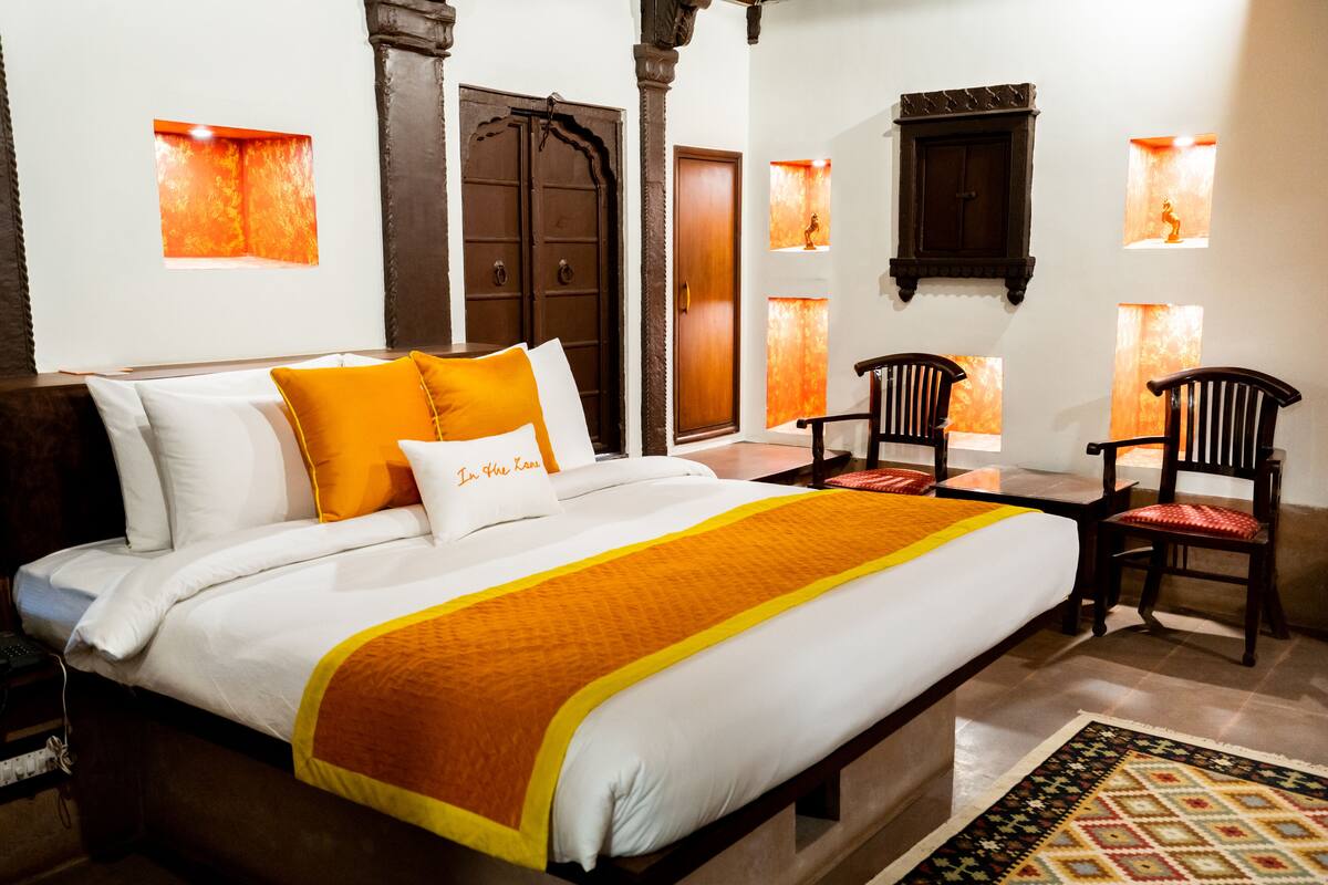 Quarto de hotel com uma cama grande, cadeiras de madeira e uma pequena mesa.