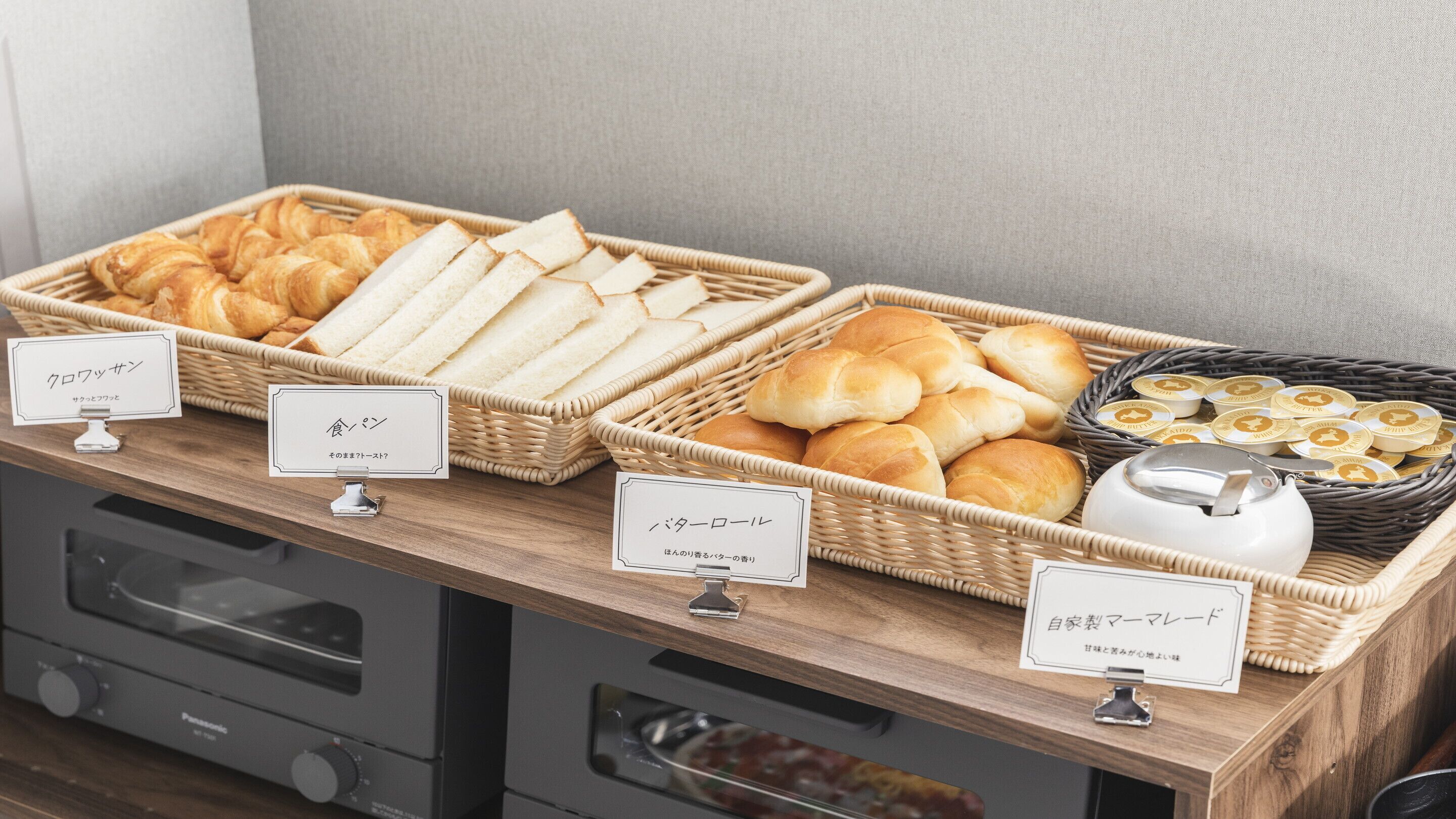 Buffet com diversos pães e pastelaria, incluindo croissants, baguetes e pães, expostos em cestos de vime.