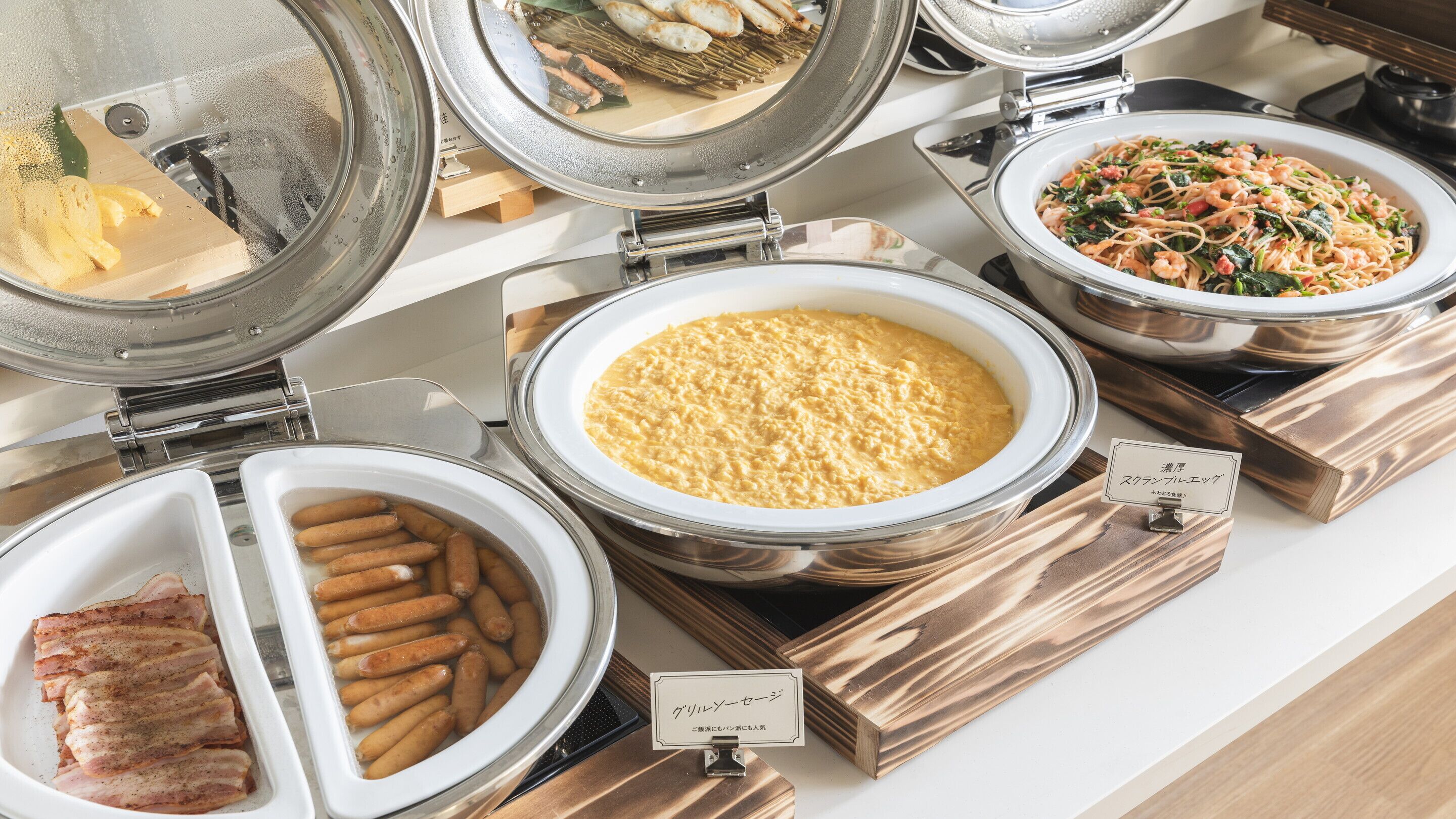 A buffet with various food options including sausages, a pasta dish, and a bowl of what appears to be cornmeal or polenta.