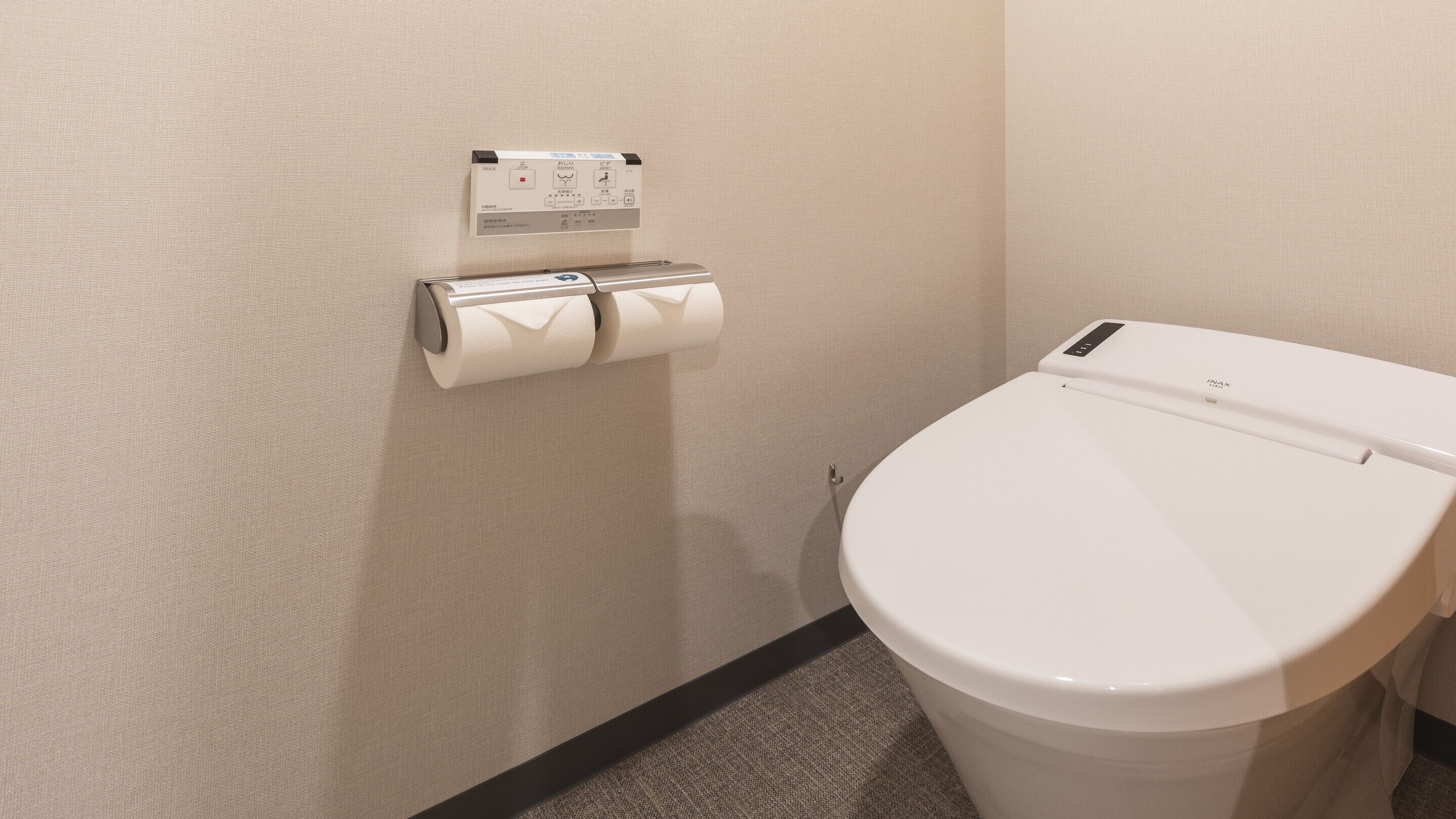 A bathroom with a toilet, a paper towel dispenser, and a wall-mounted control panel.