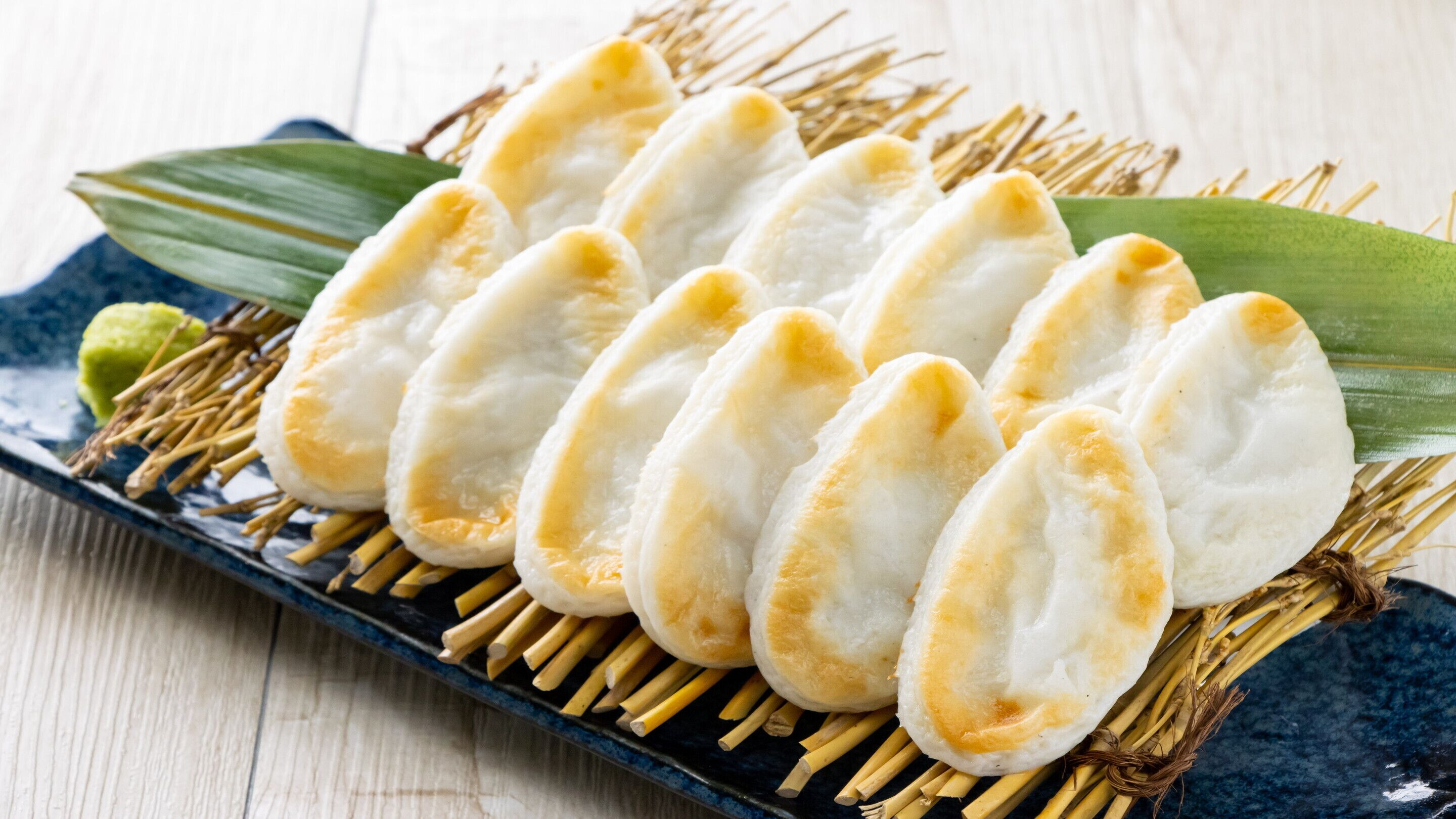 A plate of steamed buns arranged on a blue ceramic plate with a green leaf and bamboo sticks.