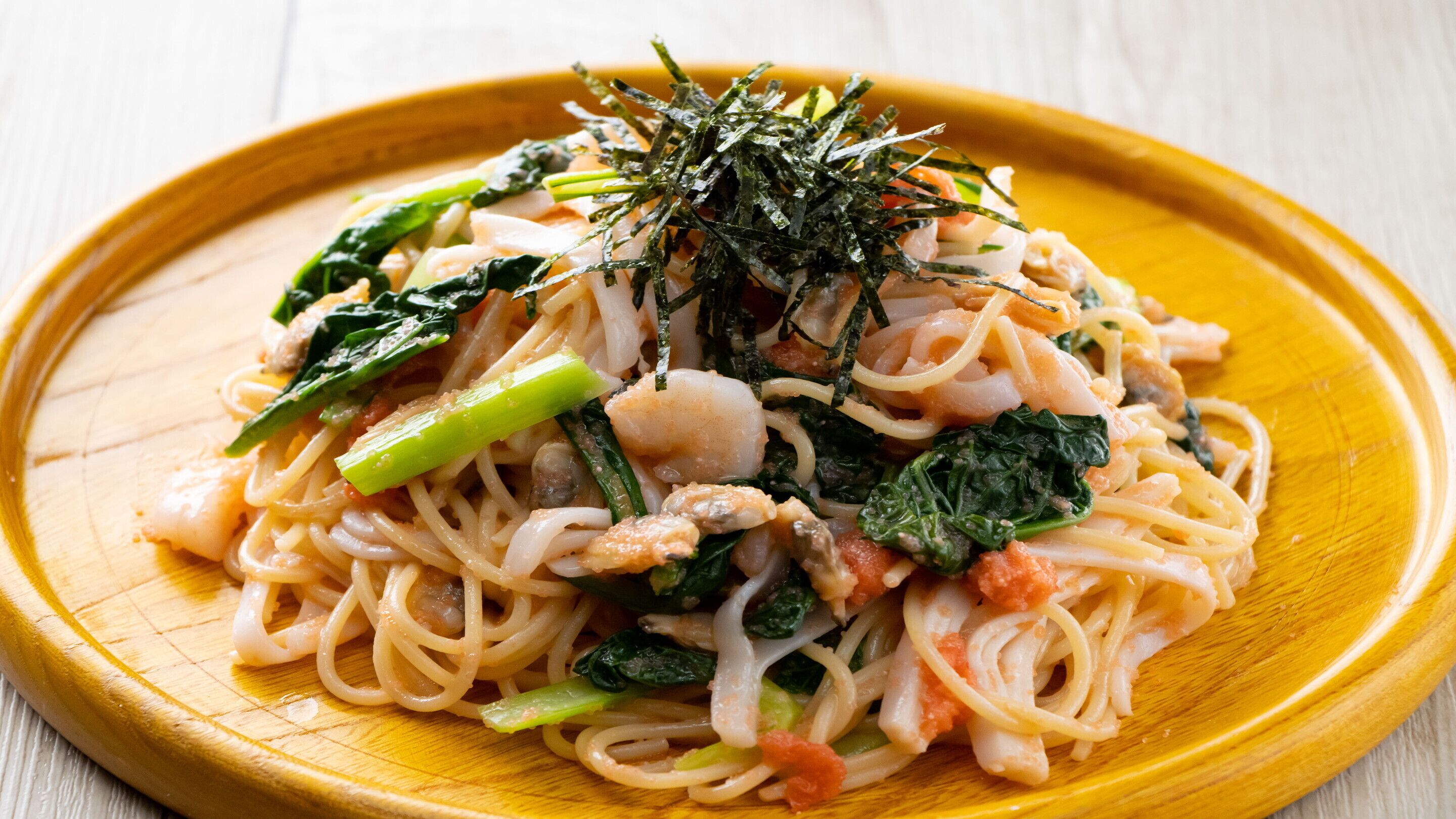 Un plato de fideos con verduras y mariscos, adornado con algas marinas.