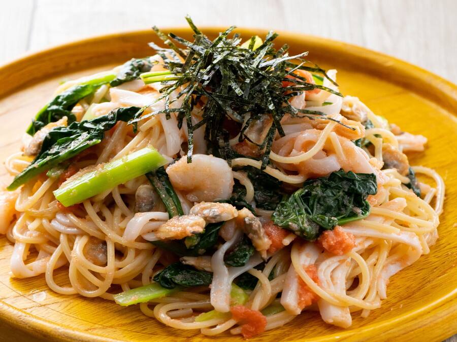 Un plato de fideos con verduras y mariscos, adornado con algas marinas.