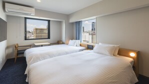 Une chambre d’hôtel avec deux lits, un bureau et une fenêtre donnant sur la ville.