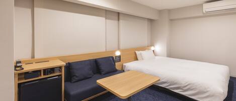A hotel room with a bed, a small desk, a sofa, and a compact kitchenette.