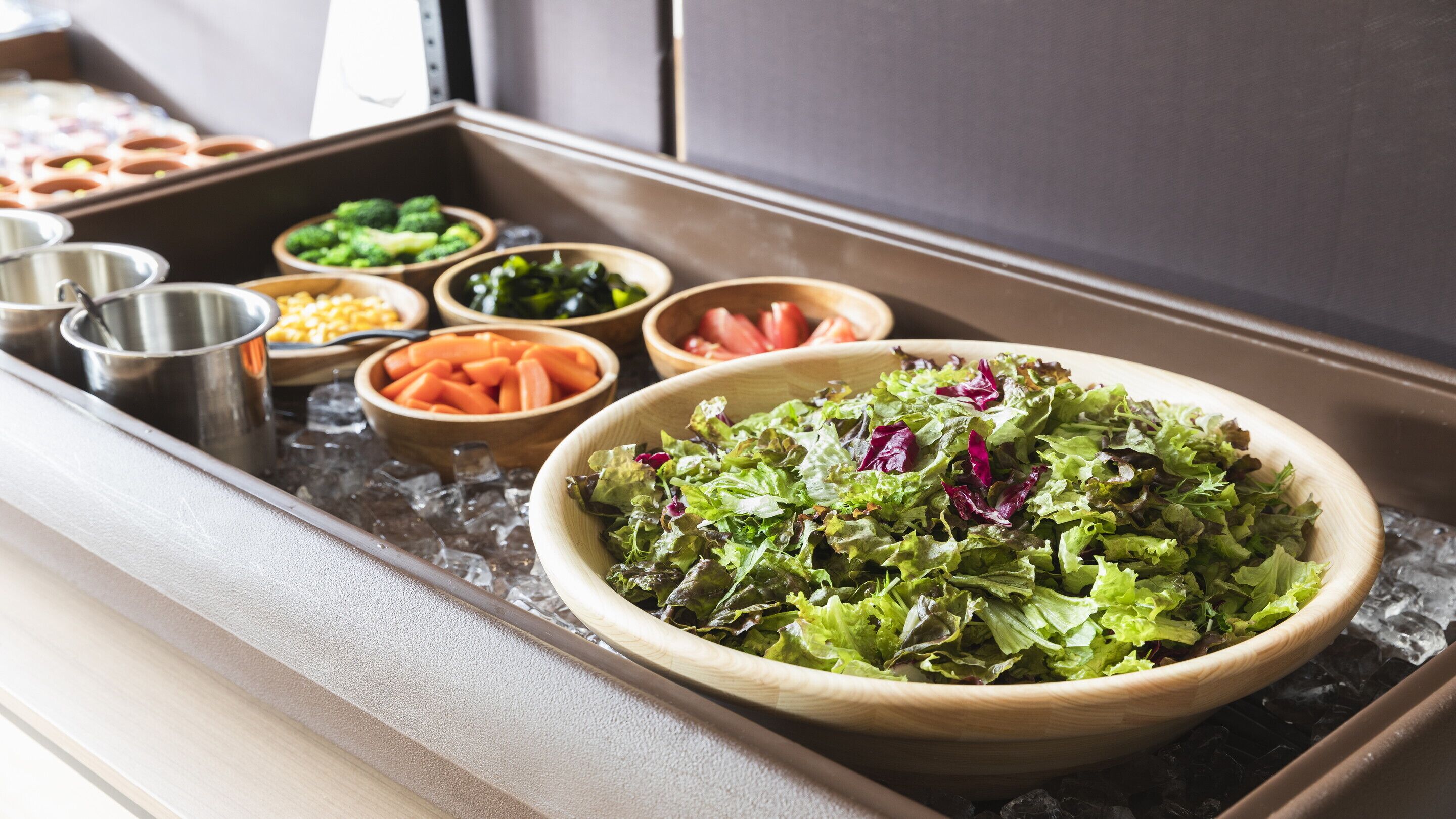 Un bufé con diversos platos, incluyendo una ensaladilla grande de verduras mixtas, tazones de vegetales y otros alimentos.