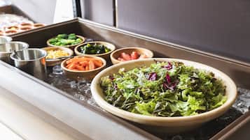 Un bufé con diversos platos, incluyendo una ensaladilla grande de verduras mixtas, tazones de vegetales y otros alimentos.